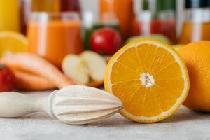 rodajas de naranja fresca con exprimidor. hacer jugo de fruta fresca. color naranja. tarros borrosos de jugo en el fondo. tiro horizontal foto