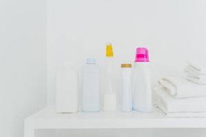 Stack of folded white towels and bottles with detergent against white background. Washing and cleanliness concept. Space for your text photo