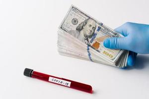 Laboratory sample of blood testing for coronavirus diagnosis, stack of money near against white background. Covid-19 economic impact. Economic crisis. photo