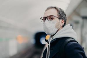 Serious man wears medical mask against transmissible disease, travels in subway, being in danger at public transportation, tries to get to work in crowded underground train. Coronavirus, Covid-19