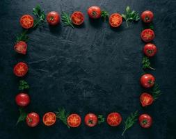 Composition of red tomatoes and green fresh parsley and dill lying on dark background in form of frame. Vegeterian food concept. Free space in middle photo
