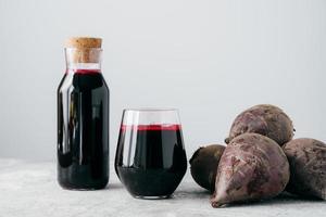 Fresh bright beetroot juice in glass bottle, raw red beet near, isolated over white background. Healthy drink. Detox natural beverage photo