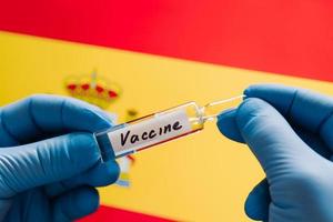 Fight against coronavirus. Medical worker develops vaccine for Covid-19. Hands in medical gloves with vaccine against Spain flag background. Health care concept photo