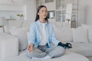 Tranquil disabled woman is sitting in lotus pose. Modern artificial limb with sensor control. photo
