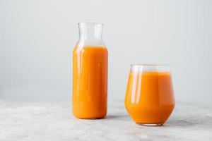 Fresh squeezed carrot juice in bottle and glass on wooden table isolated over white background. Vegetable beverage. Healthy drink. photo