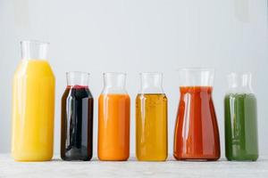 Glass bottles of fresh multicolored drinks standing in row on white background. Fruit and vegetable juice for you to drink. Healthy beverage photo