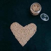 Dry clean chickpeas in glass jar. Heart made of organic uncooked garbanzo. Black background. Plant based protein. Beans for making healthy dish photo