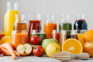 toma horizontal de frutas y verduras frescas en mesa blanca, frascos de vidrio de jugo y exprimidor de naranja. concepto de bebidas saludables. bebidas organicas foto