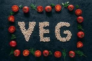 Photo of tomatoes frame and chickpea letters meaning veg. Organic seeds inside of vegetable frame isolated over dark background. Vegeterinarism
