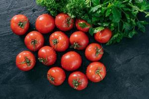 Spring vitamins concept. Harvested red heirloom tomatoes and green parsley isolated over dark background. Fresh vegetables for making salad photo