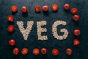 Top view of red ripe tomatoes in form of frame and letter shaped chickpeas on dark background. Vegan food concept. Organic nut. Vitamin photo