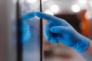 Cropped shot of mans hand in latex medical glove, uses touchscreen, checks information during quarantine pandemic coronavirus, enters pin code on self checkout. Hygiene and virus prevention concept photo