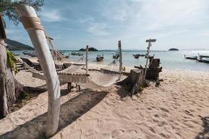 Rope cradle swing hanging on wood on the beach with wooden boat in tropical sea photo