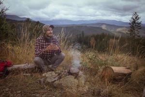 Young male traveler drink tea near campfire in mountains photo