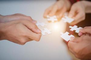 Hands of business people wearing casual plaid shirt hold paper jigsaw puzzle and solving puzzle together,Business team assembling Jigsaw puzzle,Business group wanting to put pieces of puzzle together. photo