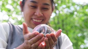 ritratto di donna asiatica che tiene in mano la sfera di cristallo e che desidera sullo sfondo verde della natura. video