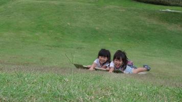 Smiling little girl sits on a cardboard box sliding down a hill at a botanical garden. The famous outdoor learning center of Mae Moh Mine Park, Lampang, Thailand. Happy childhood concept. video