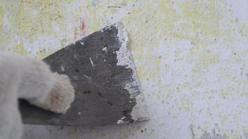 close-up da mão do trabalhador raspando a tinta velha na parede de concreto com uma espátula de metal. renovação e pintura de paredes em casa. preparação para pintar um quarto