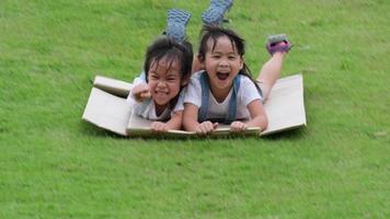 une petite fille souriante est assise sur une boîte en carton glissant sur une colline dans un jardin botanique. le célèbre centre d'apprentissage en plein air du parc minier mae moh, lampang, thaïlande. concept d'enfance heureuse. video