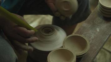 Close-up of a woman working on a potter's wheel making clay objects in pottery workshop. Female hands handle the edge of a ceramic bowl with sandpaper to reduce the sharpness before applying paint on video