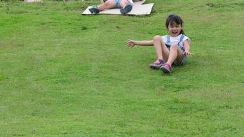glimlachend klein meisje zat en gleed van een heuvel in de tuin. gelukkig kindertijdconcept. spannende buitenactiviteiten voor kinderen. video
