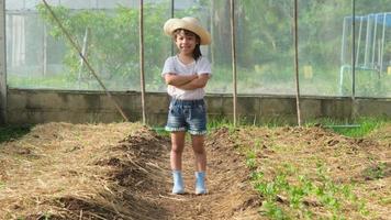 liten flicka som bär hatt hjälper sin mamma i trädgården, en liten trädgårdsmästare. söt flicka som leker i grönsaksträdgården. video