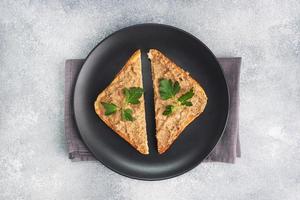 Sandwiches crispy toast and chicken liver pate with parsley leaves on a black plate. on a gray concrete table. Copy space. photo
