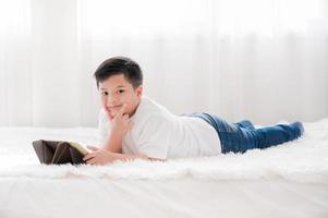 un niño asiático está acostado en una cama mientras usa una tableta para la educación en casa foto