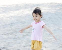 Portrait of happy charming 4 years old cute baby Asian girl, little preschooler child smiling and spreading hands, have fun on white sand background. Freedom concept. photo