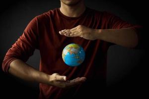 Hand of a man protecting a globe floating between his hand on black background. Earth day concept with low key tone photo