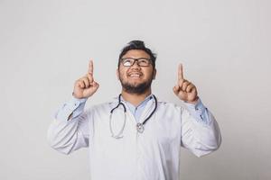 Cheerful male doctor pointing with both hands up isolated on white background photo