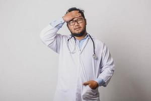 médico con expresión estresada y cansada acariciando la frente y cerrando los ojos aislado sobre fondo blanco foto