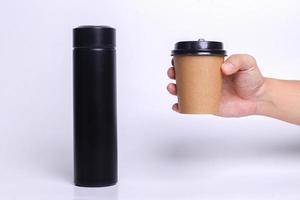 Hand holding paper cup with black thermos tumbler isolated on white background. Realistic set mock up for branding,  template for your design, presentation, promo, ad. photo