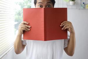 Man peeking and covering his face from behind red book for book mock up photo