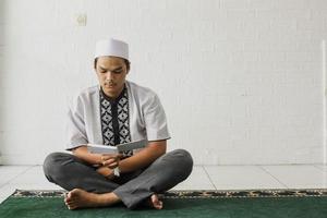 Portrait of a religious muslim man wearing a koko shirt reading the Koran seriously in the mosque photo
