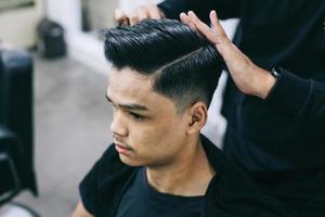 Young man at barbershop. Shave hair with the help of a hairdresser. Self-care, masculine beauty. Barber. Modern hair style photo