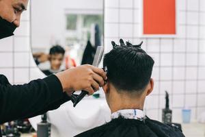 Back view of hairdresser shaving consumer's hair with clipper. photo