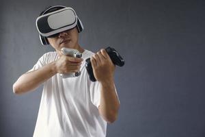 Asian man seriously playing games using VR googles and consoles againts dark grey background. Copy space for games production concept. photo