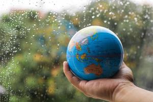 Hand holding globe on blurred rain water background. Earth day concept photo