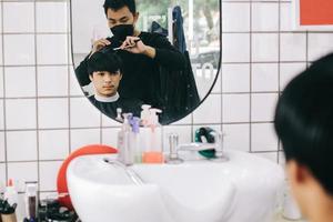 reflejo del espejo de los jóvenes en la barbería. peluquero peinando el cabello de su cliente en el salón. autocuidado, belleza masculina. Barbero. foto