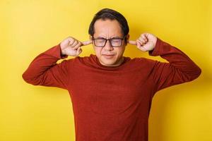 Casual man in glasses covering ears with fingers isolated on yellow background. Annoyed Expression photo