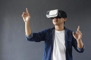 Young man using virtual reality goggles, his hands is touching or clicking isolated on dark grey background. Copy space for futuristic business, education and games concept. photo