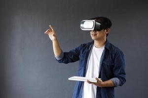 Smiling man using virtual reality goggles and wireless keyboard, he enjoying the games as if touching or clicking digital screen. Copy space for futuristic business, education and games concept. photo