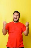 Atrractive young fat Asian man raising his fists with mouth yelling face, yes gesture, celebrating success, photo