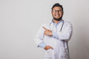 Cheerful male doctor with sideways pointing gesture at copy space isolated on white background photo