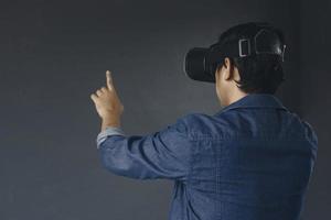 Side view of young man in casual style wearing virtual reality googles, his finger pointing out or touching blank screen. Copy space for futuristic games and education concept. photo