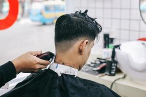 vista posterior del peluquero afeitando el cabello del consumidor con una maquinilla. foto