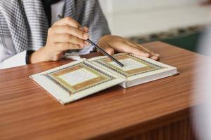 Close-up portrait of muslim man hands pointing at letters while reading the Quran with a stick on a wooden table photo