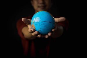 Hand of a man giving a globe on a black background. Earth day concept with low key tone photo