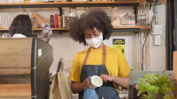 la barista afroamericana trabaja limpiando la taza de café, mirando a través de la ventana del café, esperando a los clientes en un nuevo servicio de estilo de vida normal, el impacto comercial de la cuarentena pandémica covid19. video